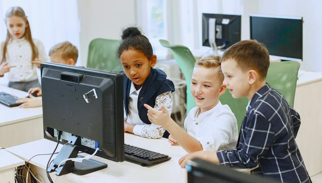 Elementary school children looking at a computer monitor in a classroom with enhanced K-12 cybersecurity measures.